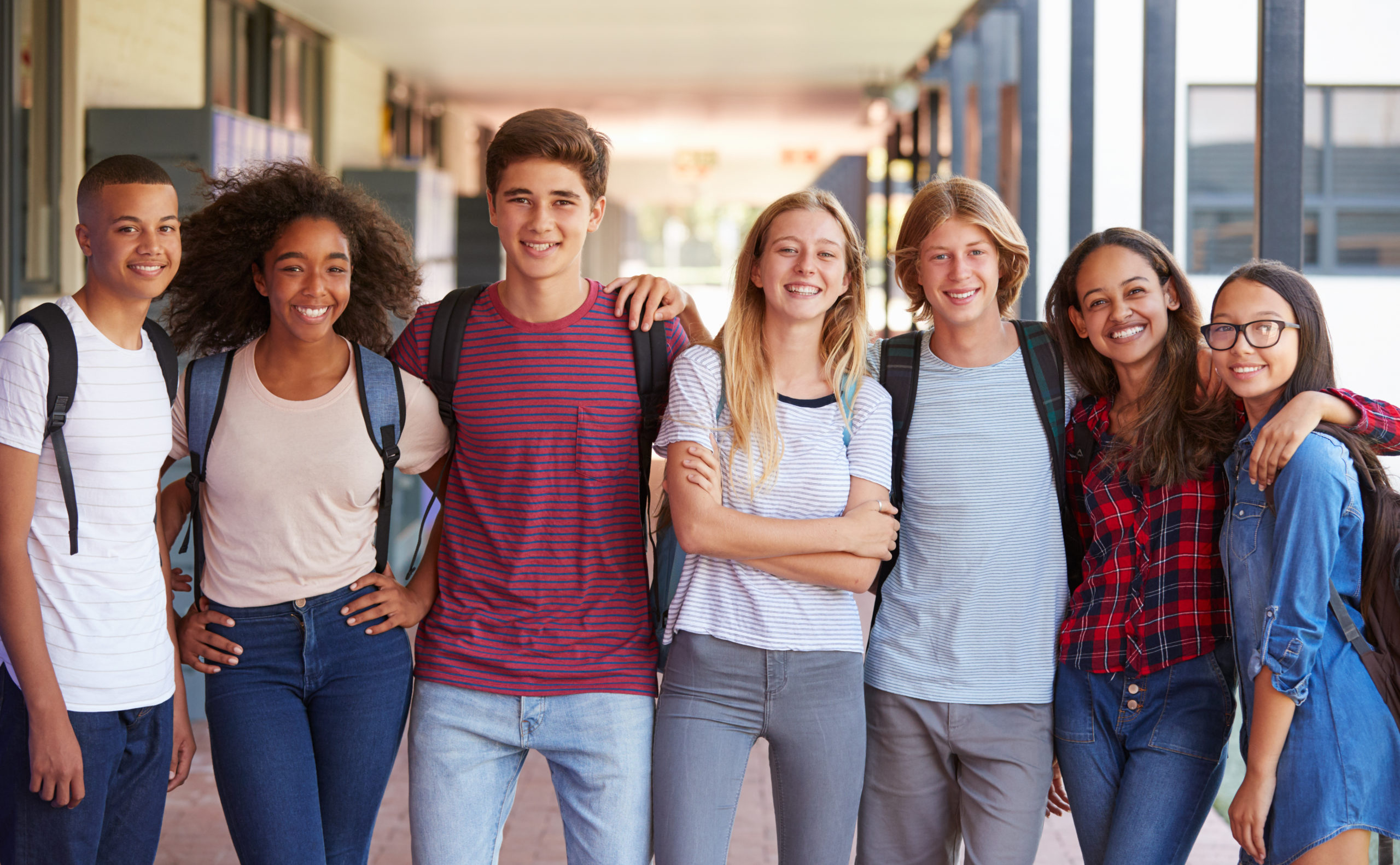 Group of high school kids standing in a hall grouped together, smiling at the camera. 