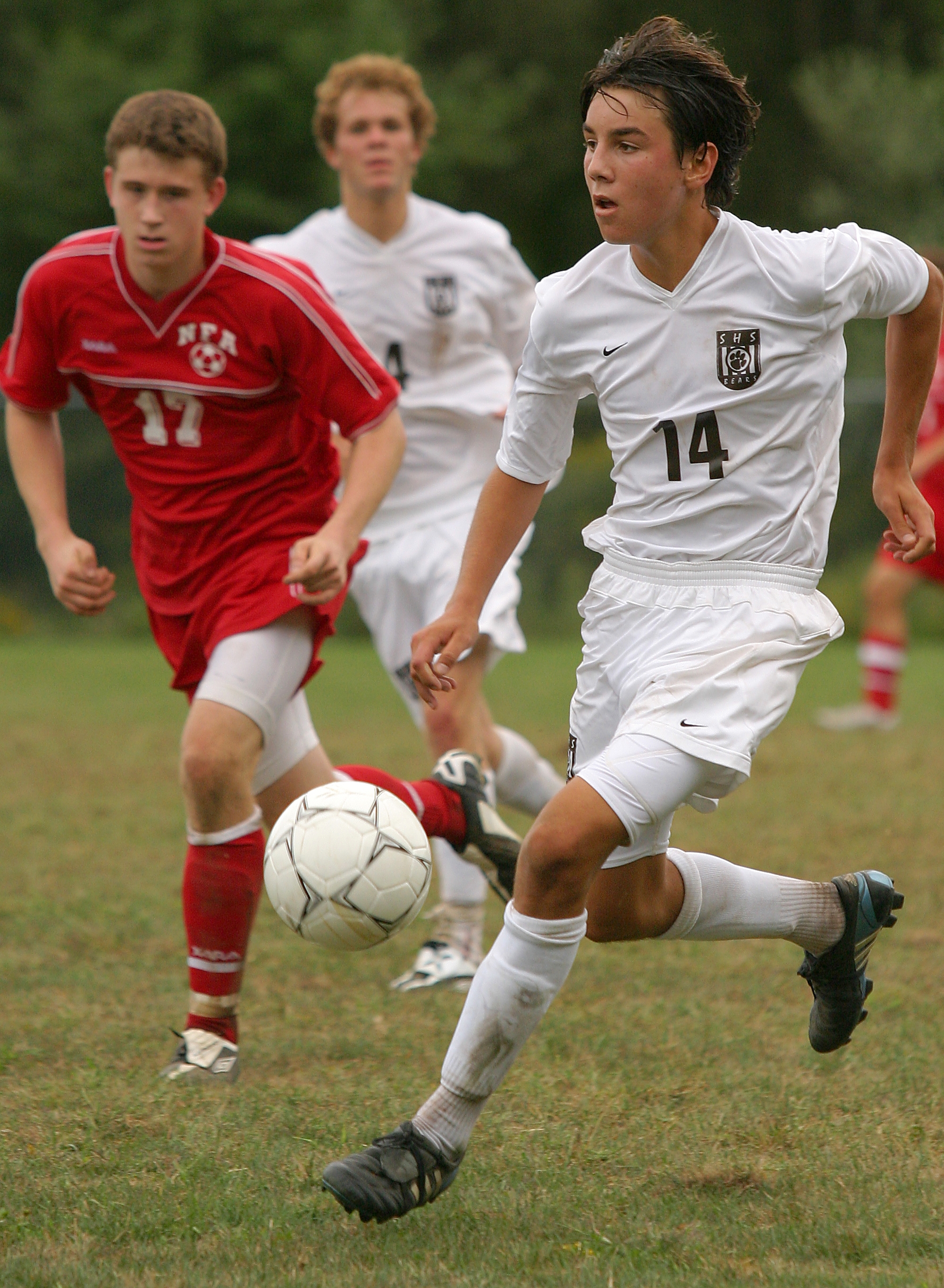 High school boys are playing soccer in white and red uniforms.
