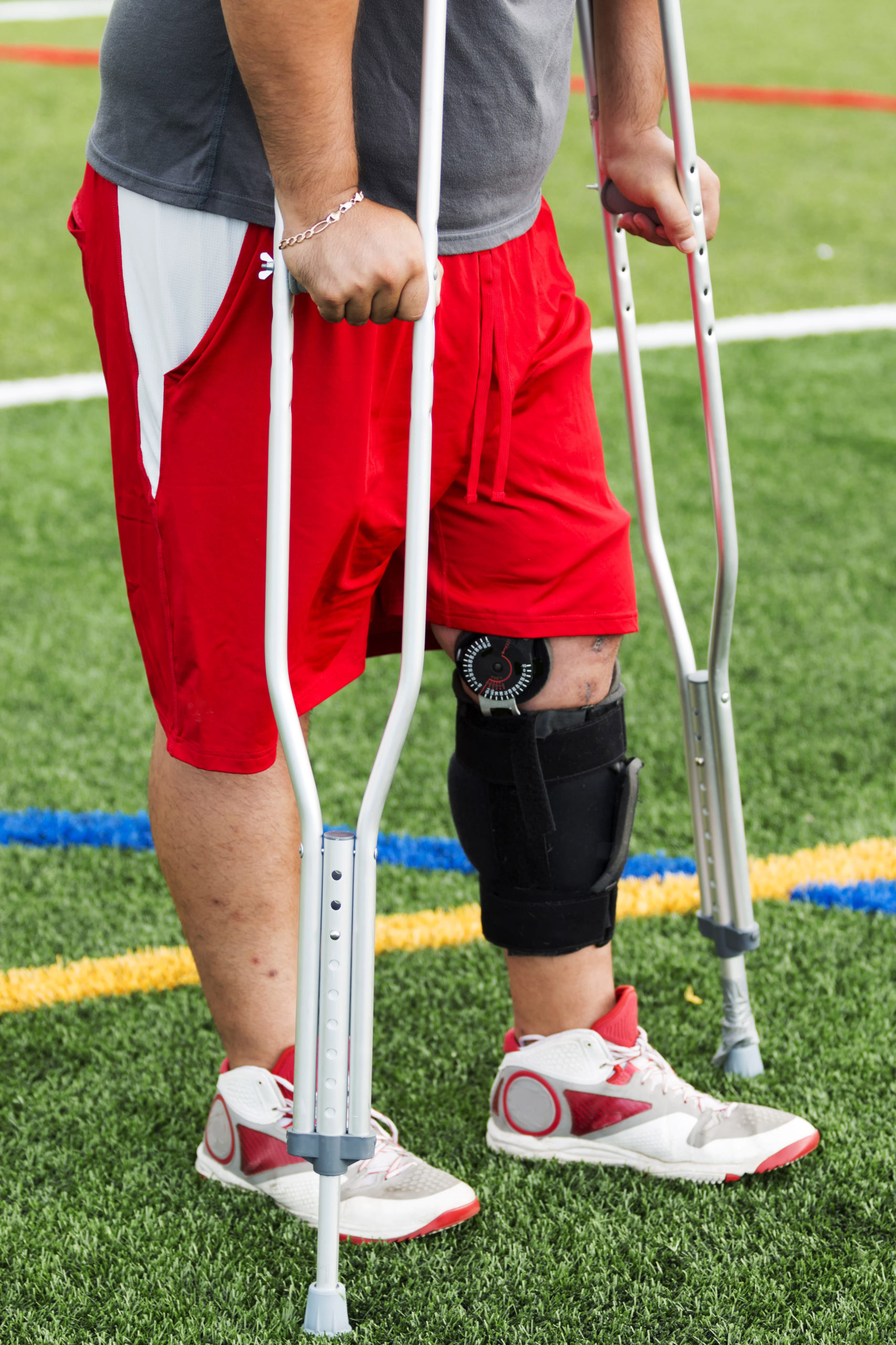 Injured male athlete on the sidelines wearing a knee brace and crutches.