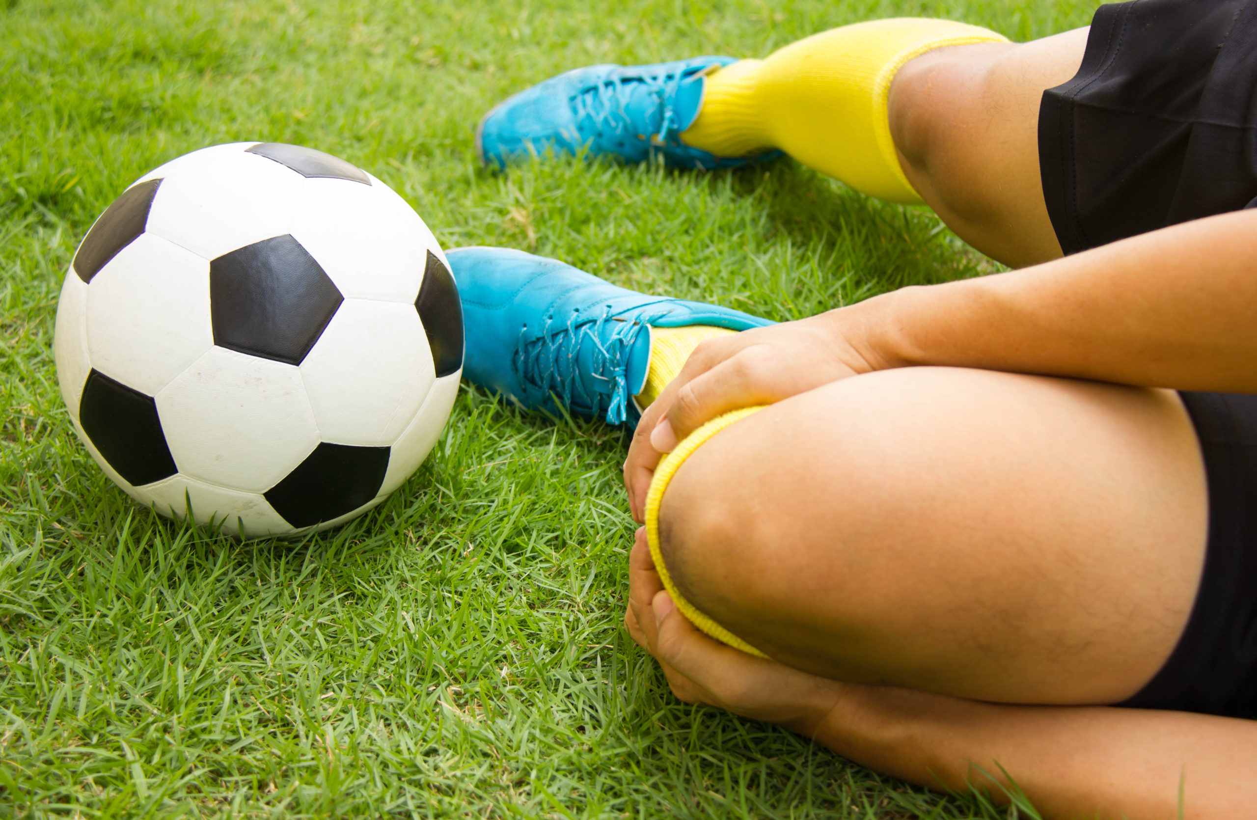 Injured player on the ground with a soccer ball next to bright teal soccer shoes. 