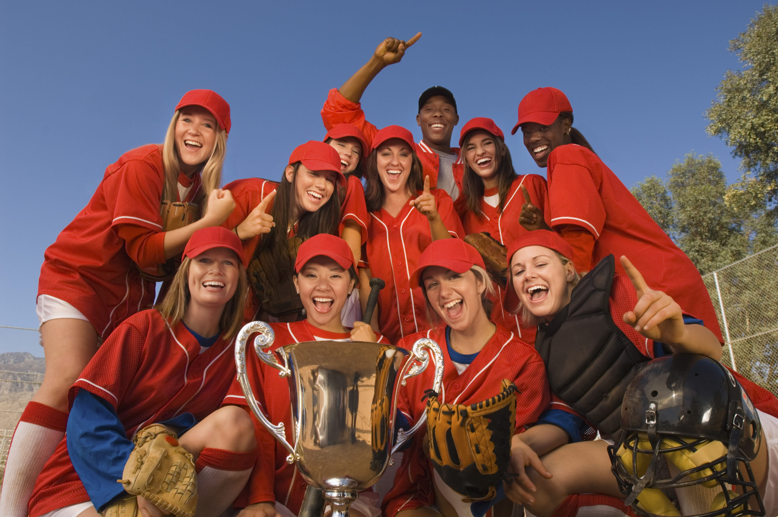 Adult rec league women’s softball team dressed in red celebrates winning a trophy.