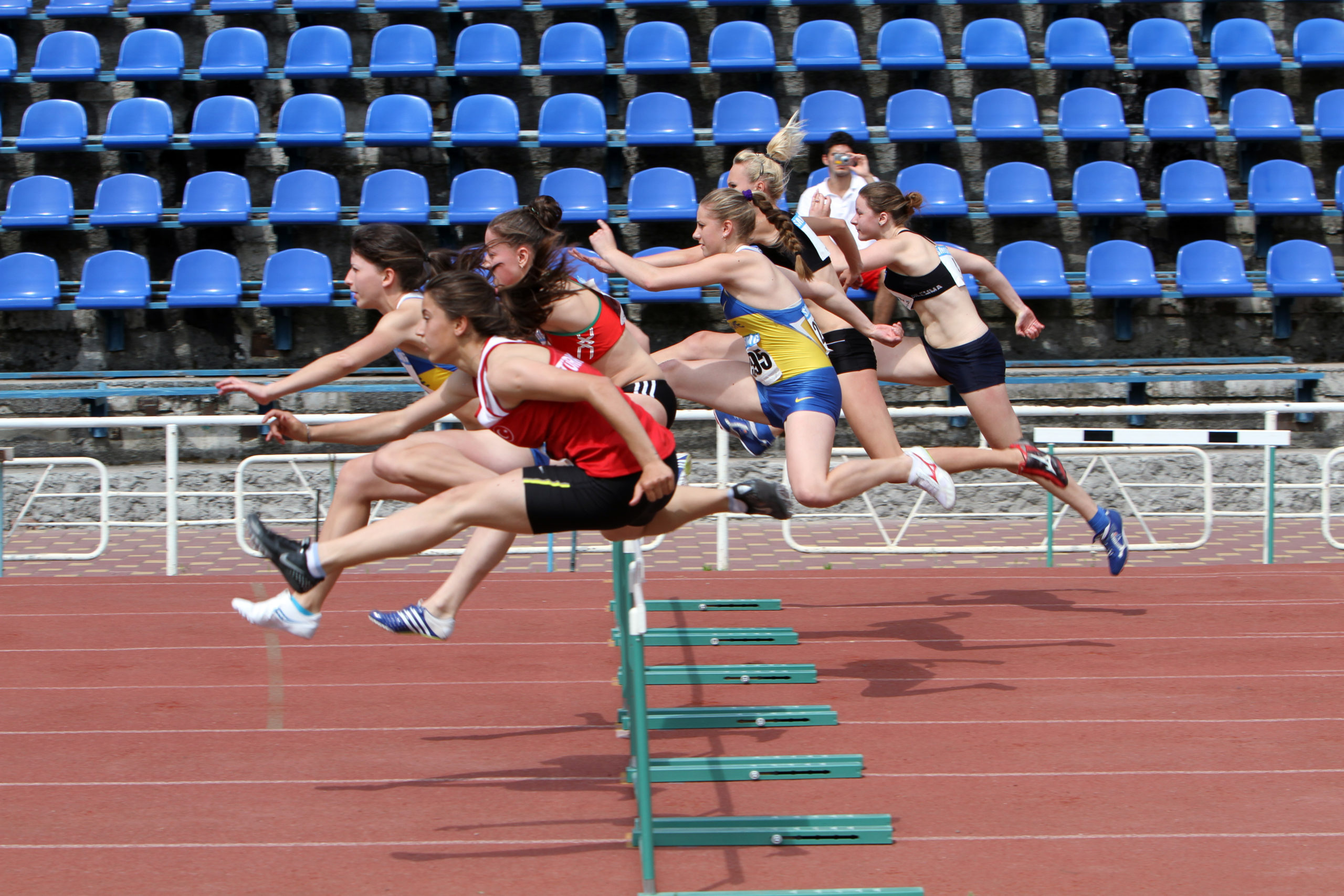 College track teams compete in a race, going over hurdles, thankful their sports injury claims are covered if they are injured. 