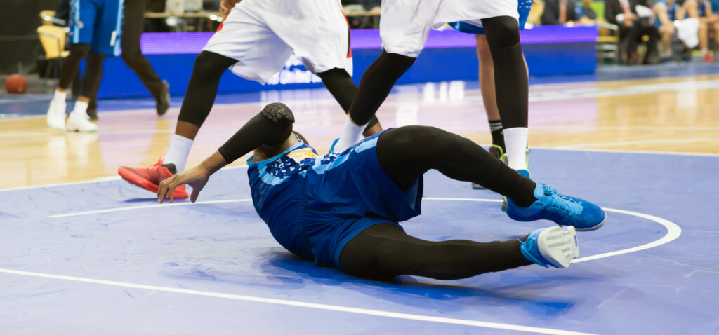 A basketball player has fallen on the court because of a common sports knee injury.