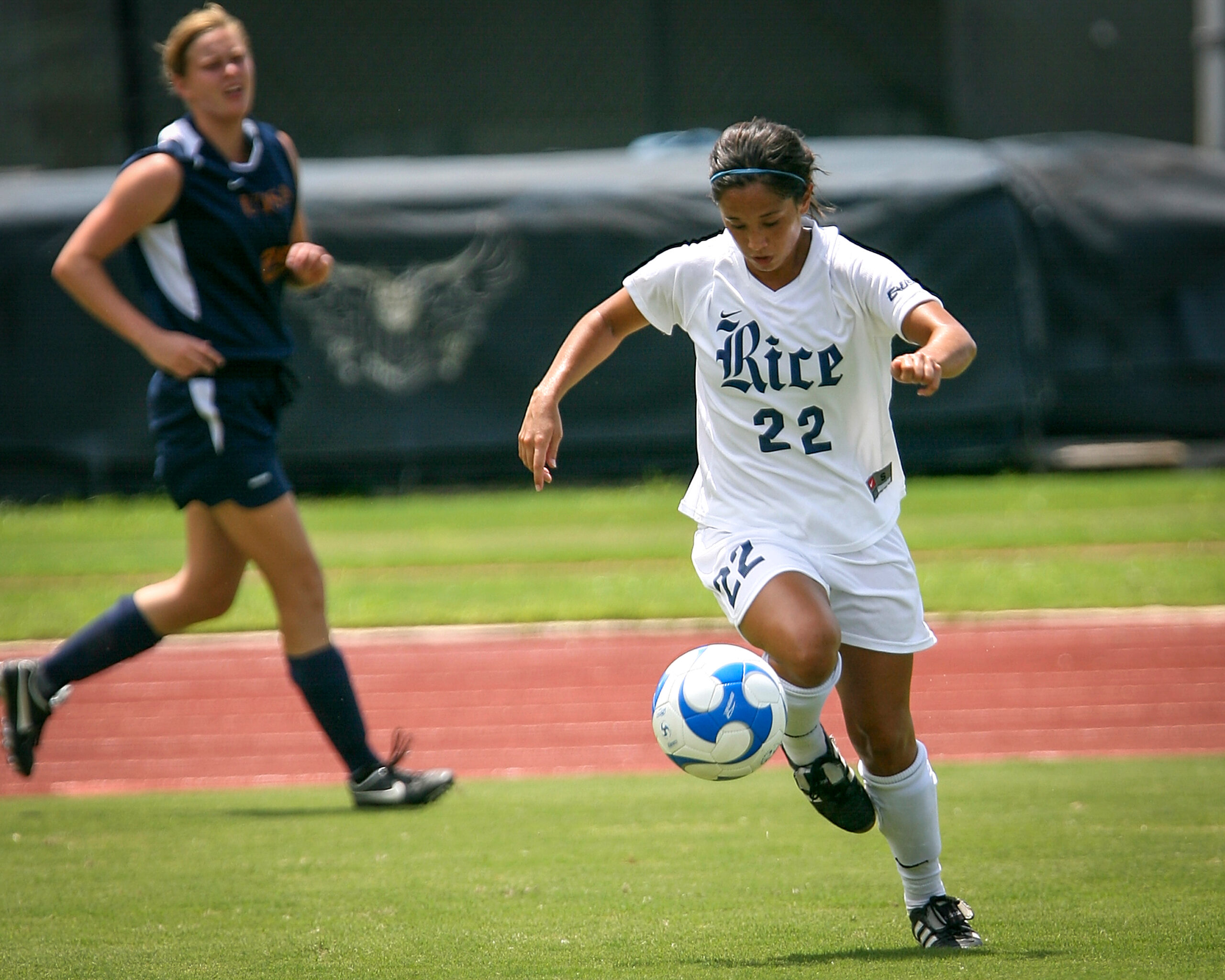 Rice women’s soccer player has the soccer ball while another player pursues her. She is protected by the college’s self-funded insurance. 