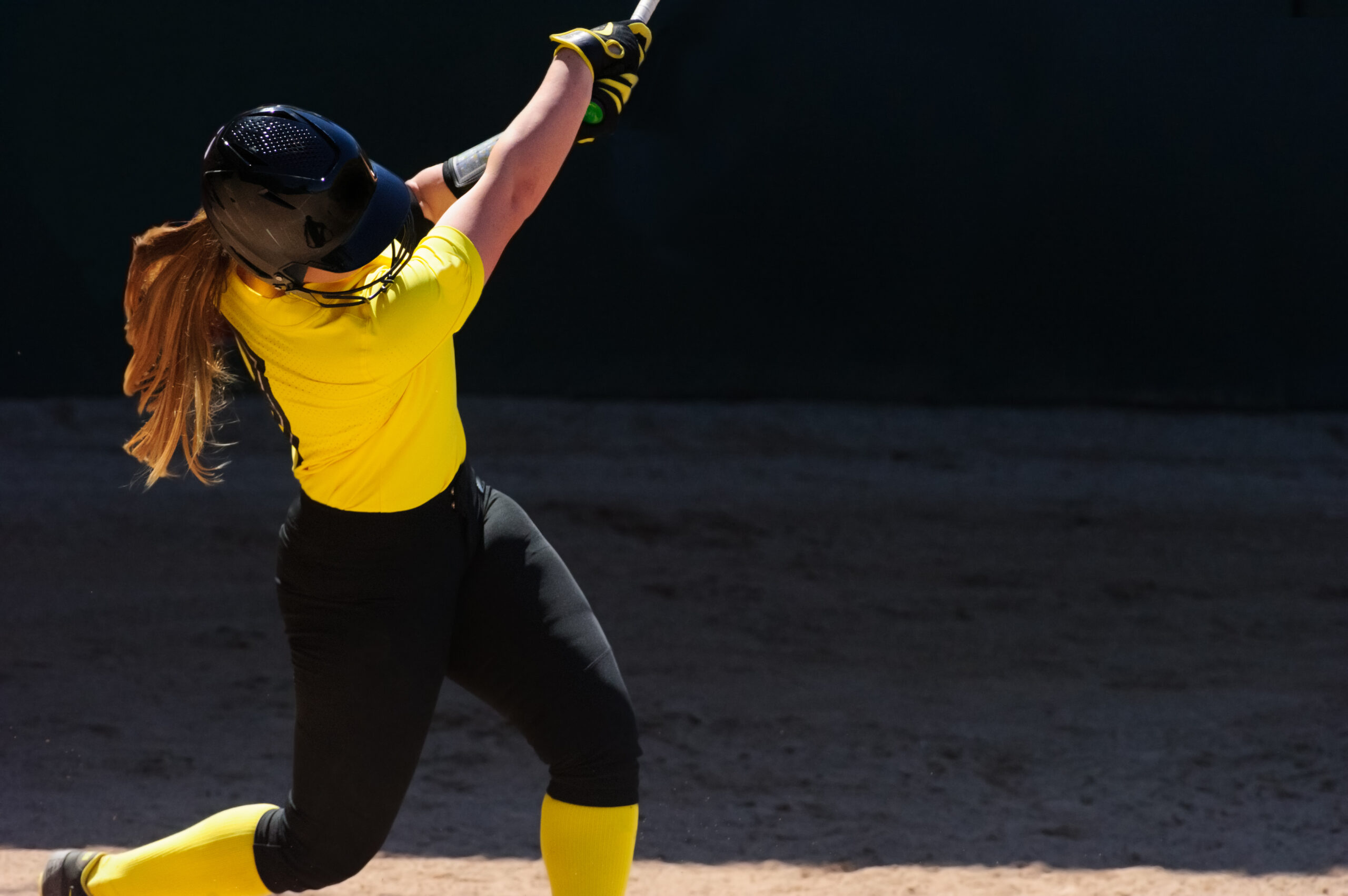  A NJCAA college softball player in a yellow jersey swings the bat while covered by the best catastrophic insurance. 