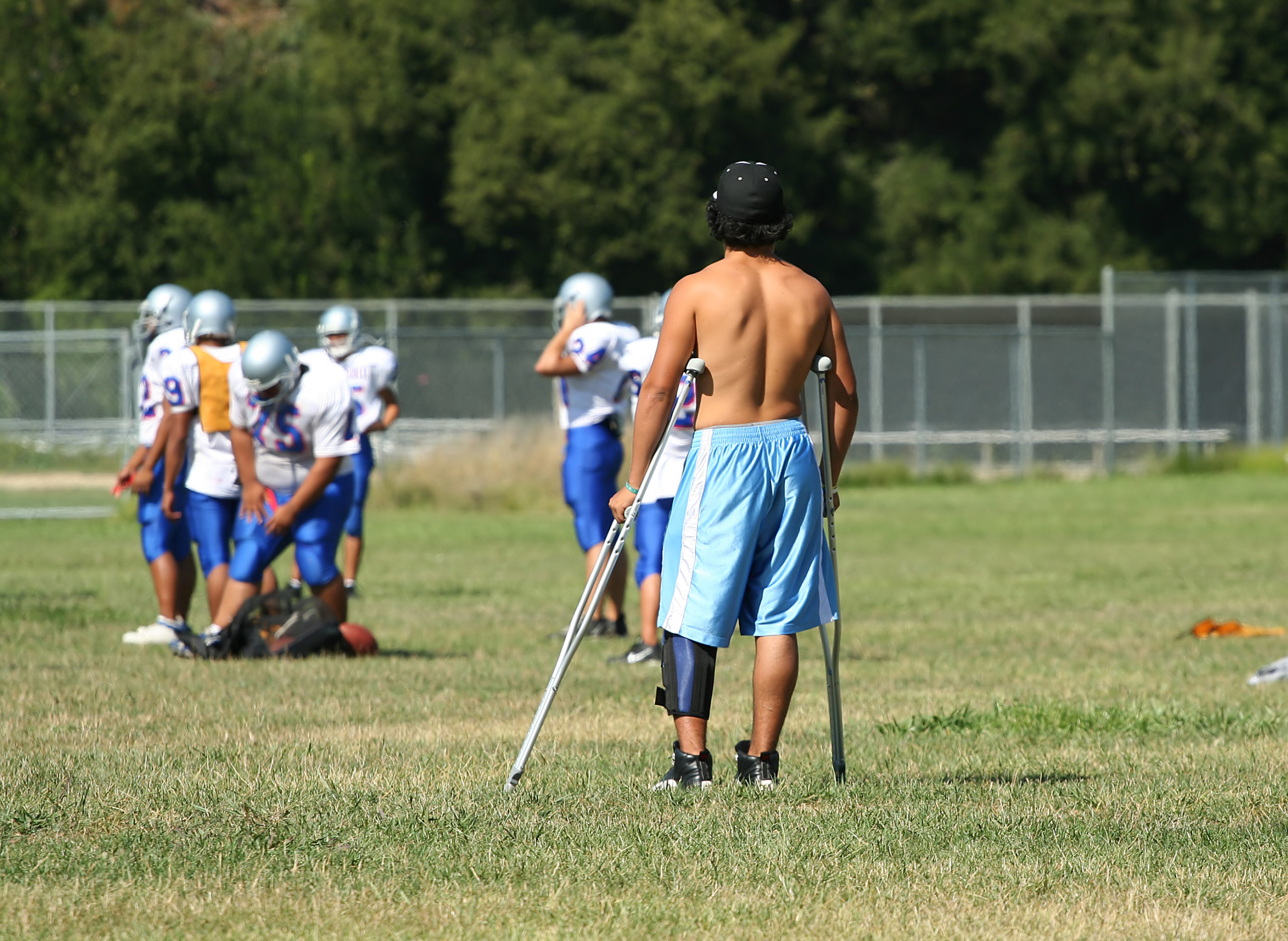  Sidelined college football player watches team practice.