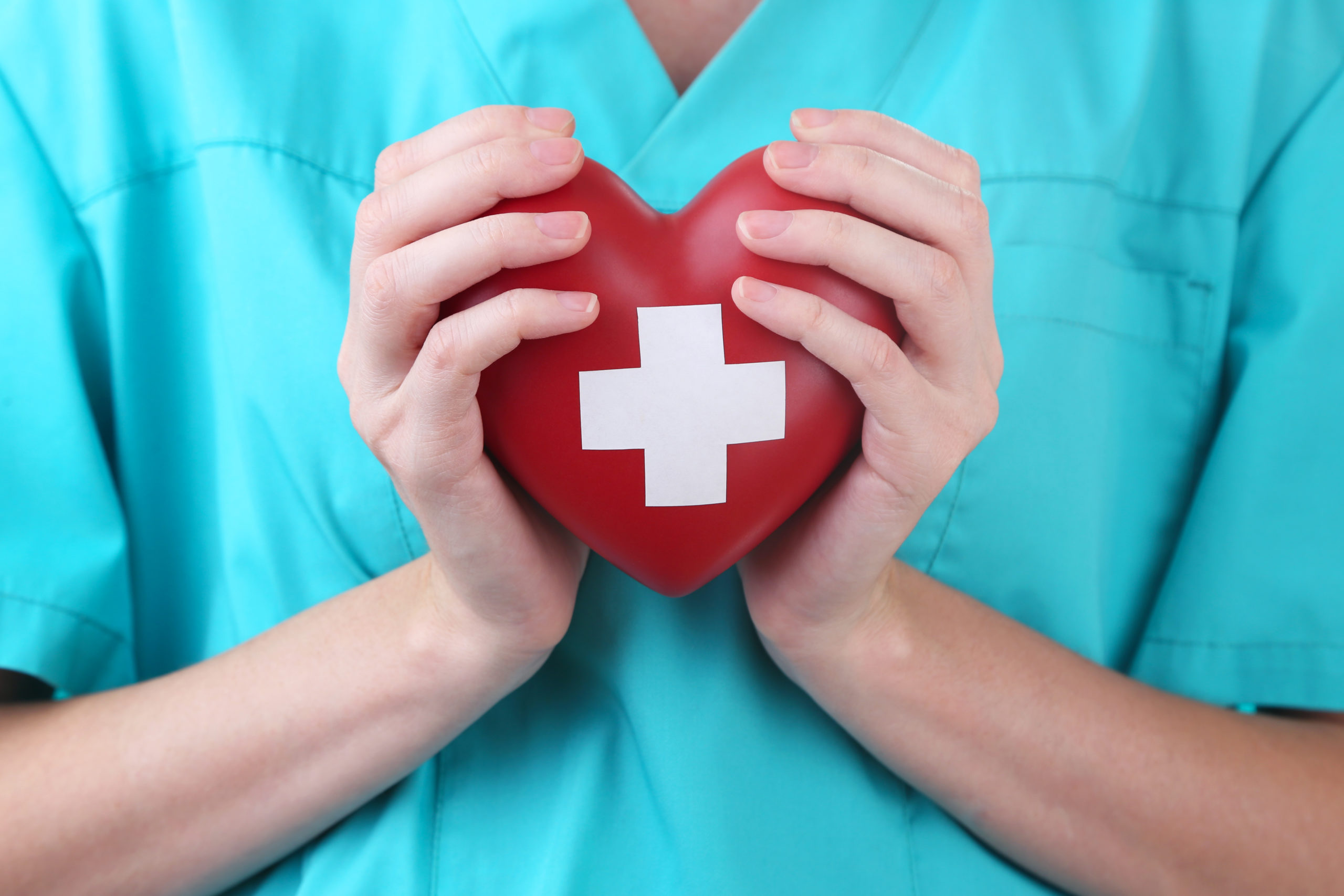 A close-up red heart with a white cross held in a doctor’s hand symbolizes athletes dying of heart attacks. 