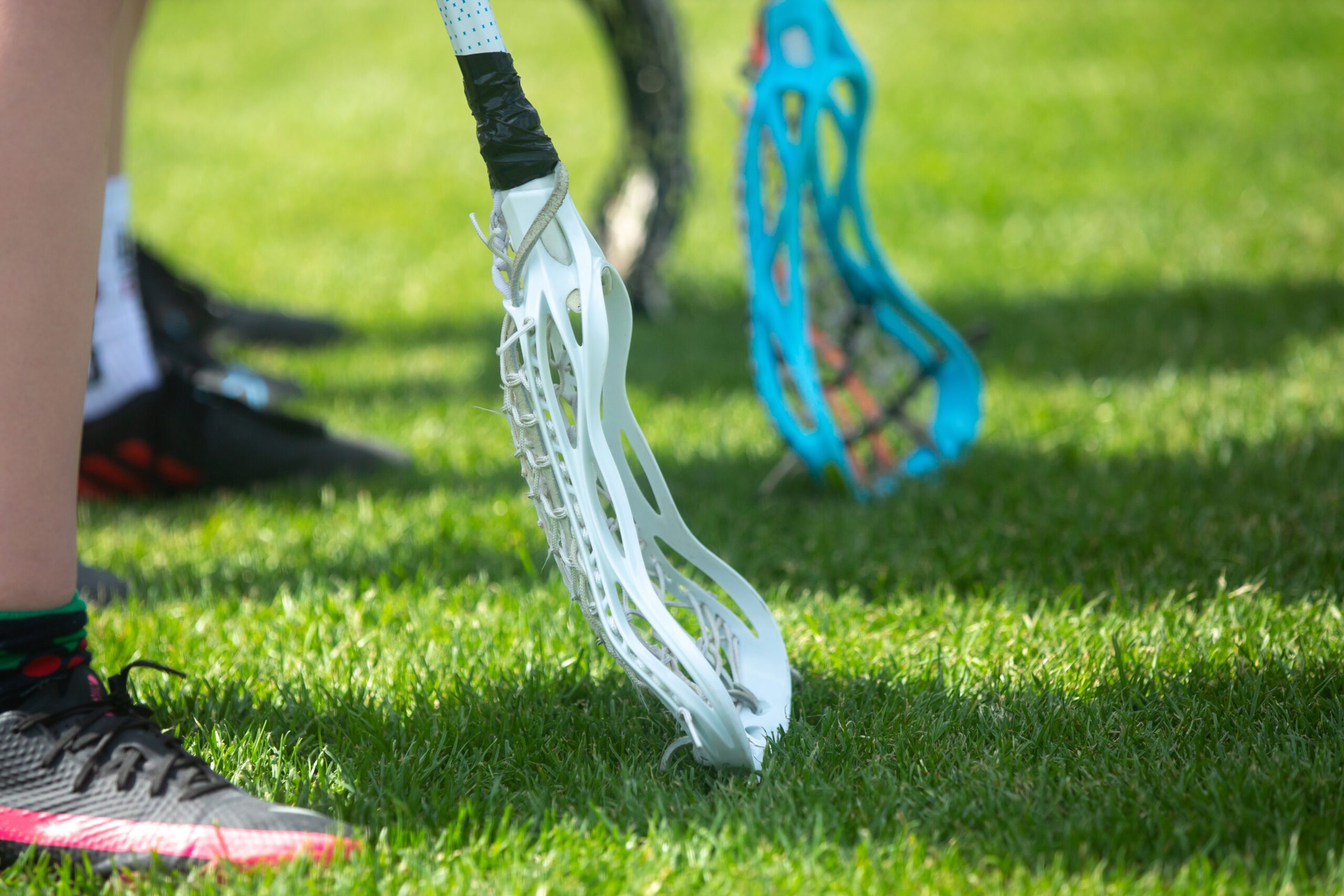 Close-up shot of women’s lacrosse sticks on the ground before the start of a match. Players are covered by the college’s self-funded insurance.