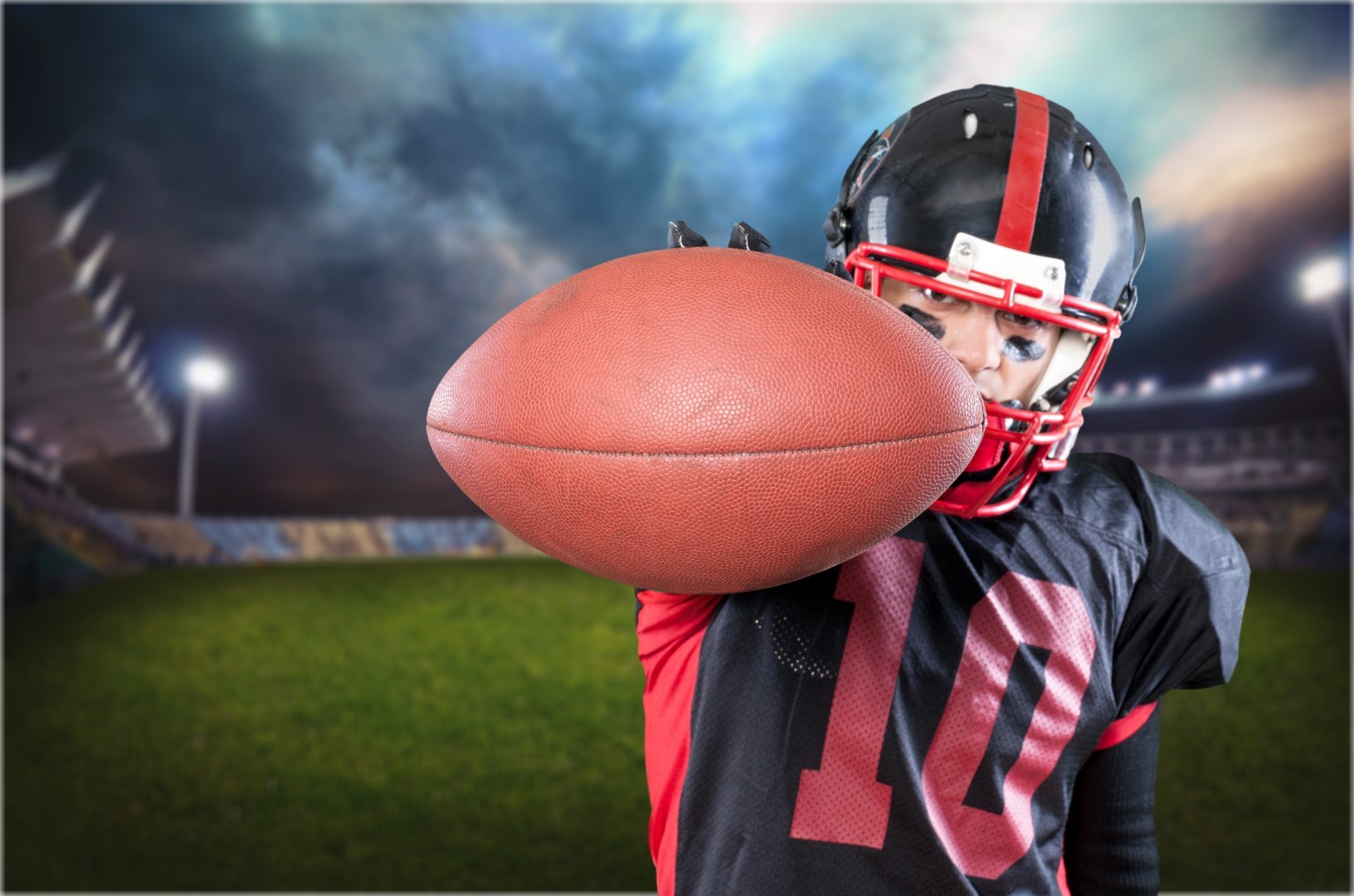 A football player wearing a black and red uniform holds a football in front of him.