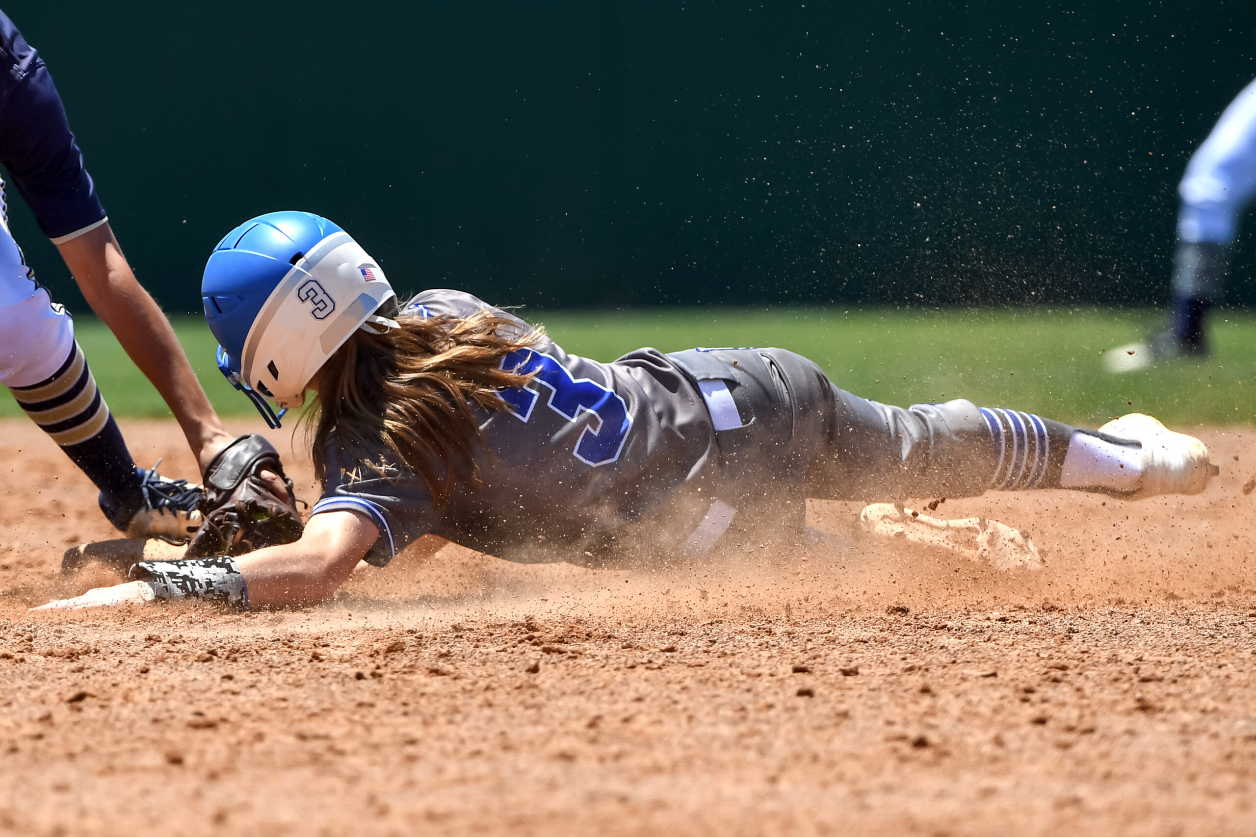 A young player at softball camp slides onto a base headfirst while protected by amateur sports insurance.