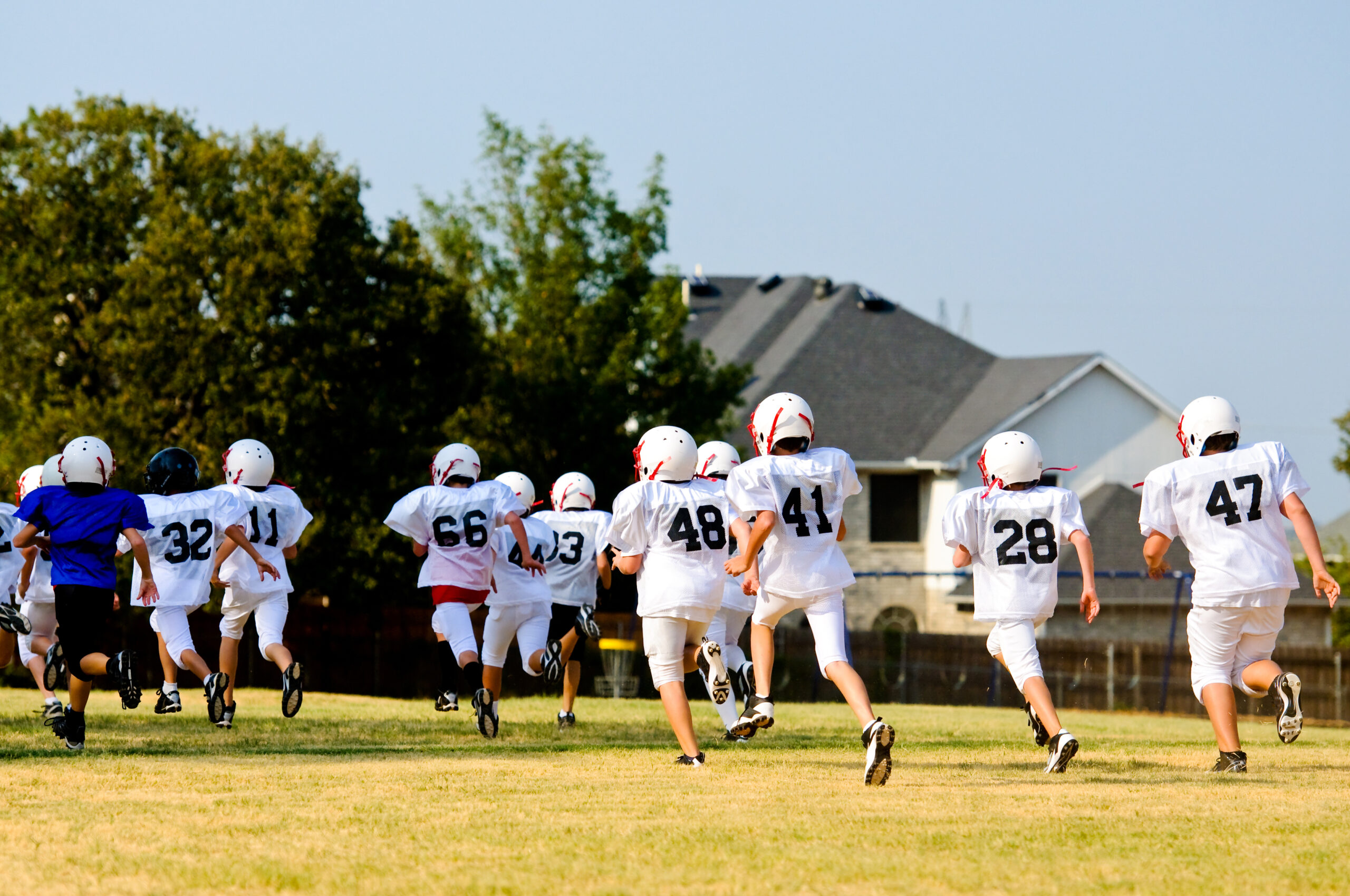 A team of young football players at sports camp gathers on the field, glad to be protected by amateur sports insurance.