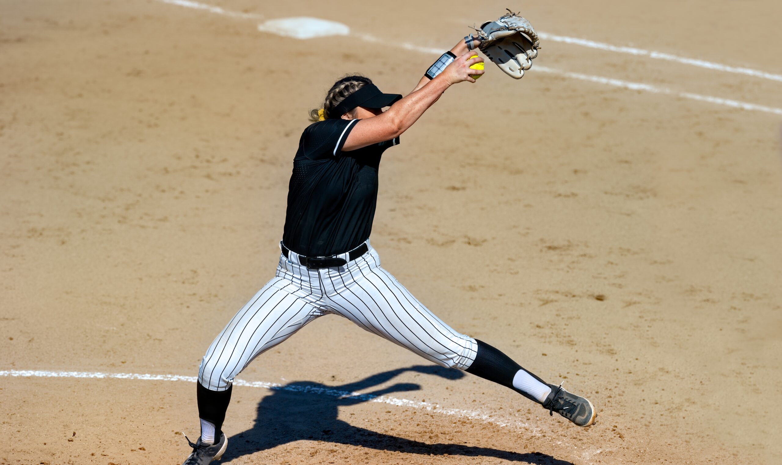 A college sports softball pitcher winds up to throw the ball to the batter. 