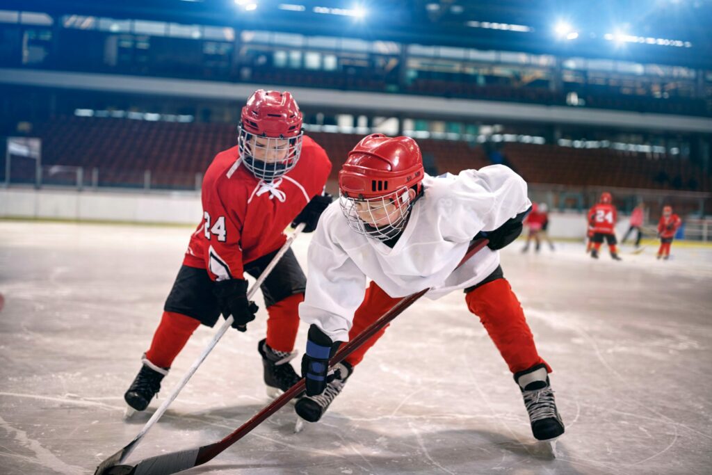 Young children in red & white uniforms play ice hockey while covered by amateur sports insurance. 