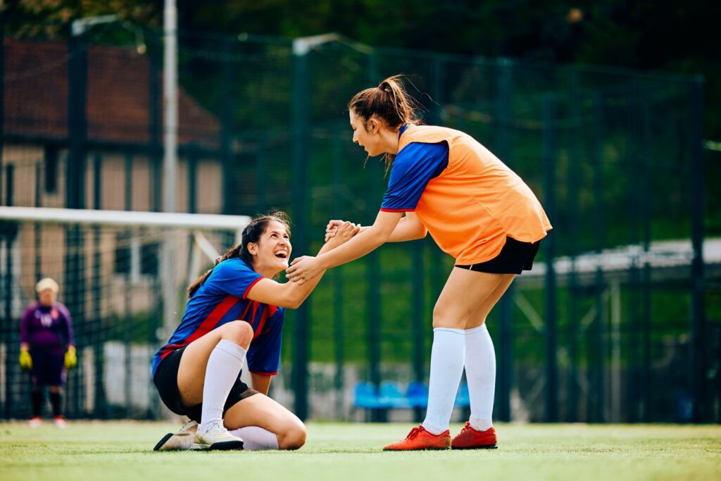 Middle school soccer player helping her opponent off the ground.
