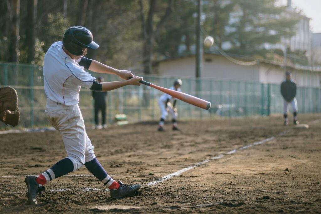 A high school batter swings at the baseball on a muddy baseball diamond.